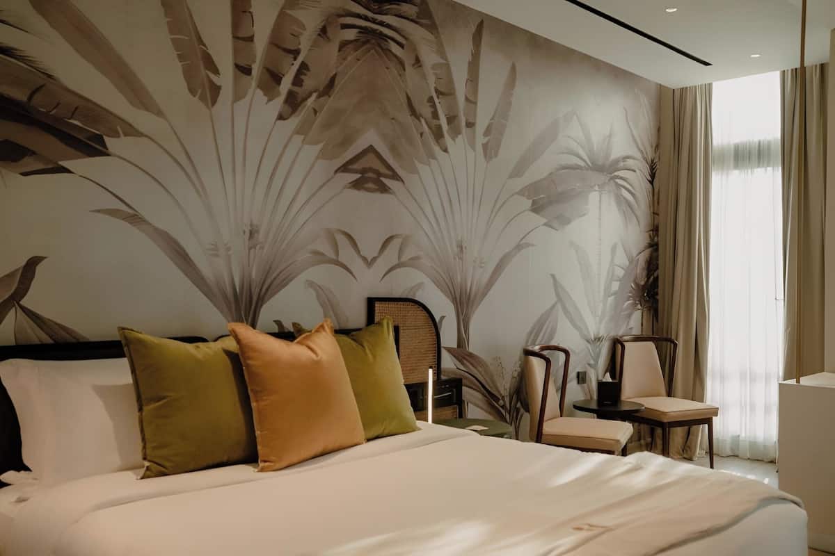 Une chambre d’hôtel moderne avec un grand lit, une chaise, une petite table et une grande fenêtre avec des rideaux.