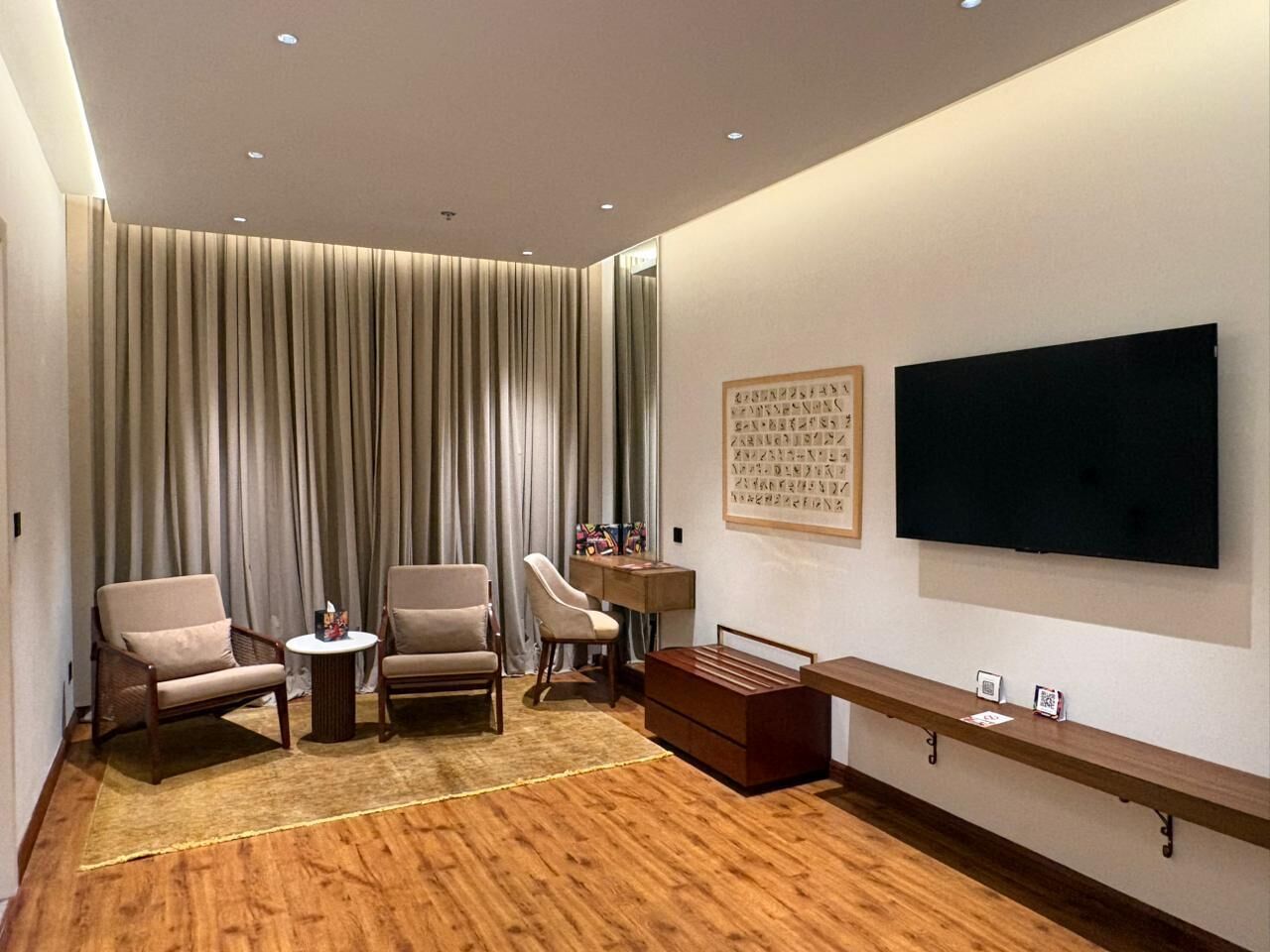 A modern living room with a flat-screen TV, two armchairs, a small round table, and a wooden bench.