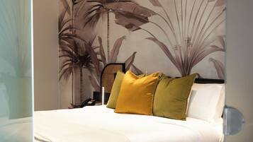 A bedroom with a bed, a headboard, a wall with a plant mural, and a nightstand.
