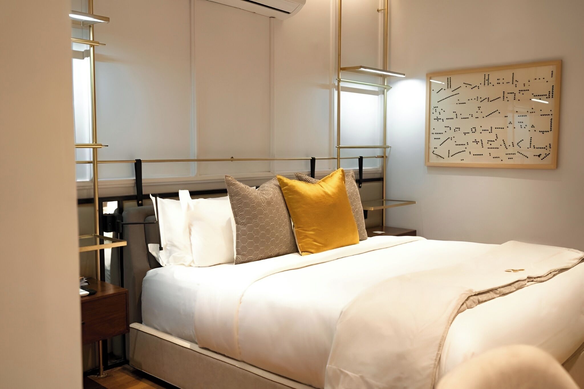 Une chambre à coucher bien aménagée, avec un lit, des tables de chevet, une œuvre d’art accrochée au mur et un luminaire moderne.