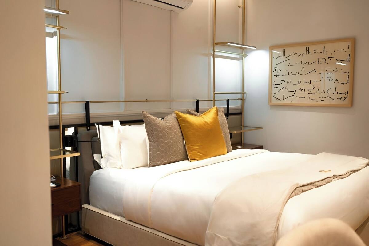 A neatly arranged bedroom with a bed, bedside tables, a wall-mounted artwork, and a modern light fixture.