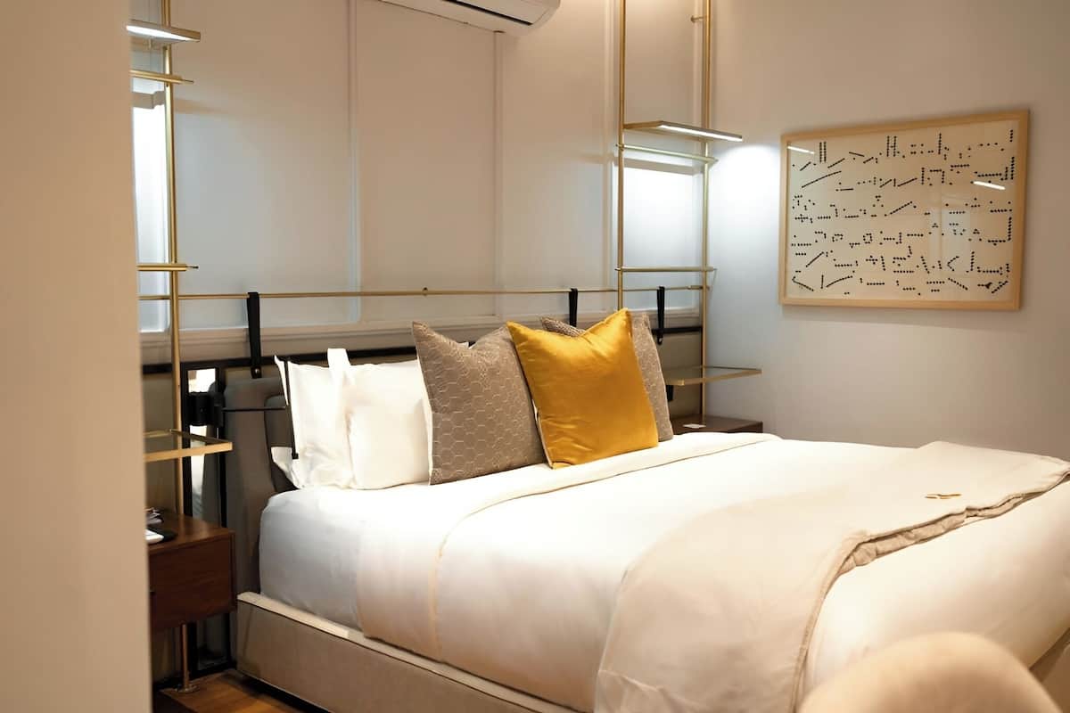 Une chambre à coucher bien aménagée, avec un lit, des tables de chevet, une œuvre d’art accrochée au mur et un luminaire moderne.