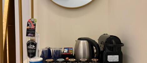 Mini bar di un hotel con una bottiglia d'acqua, una confezione di Pringles, una macchina per il caffè, un bollitore e diversi vasetti di condimenti.