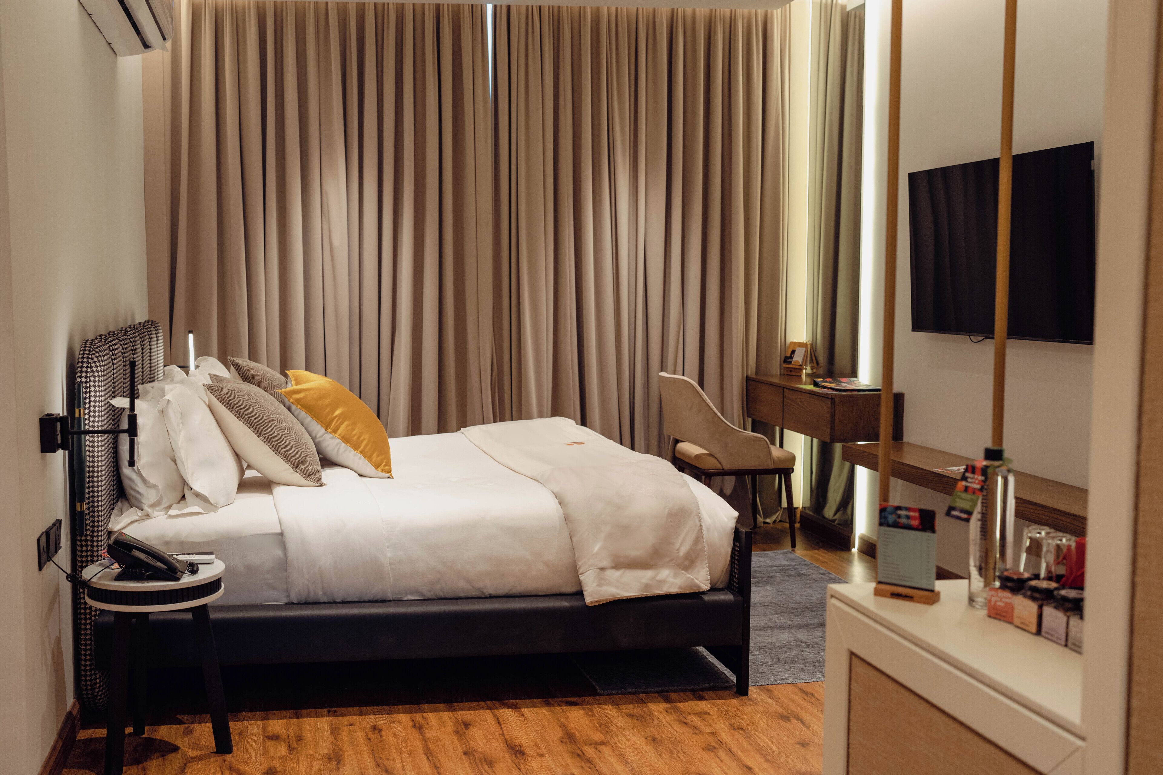 A hotel room with a bed, bedside table, lamp, chair, desk, and a flat-screen TV.