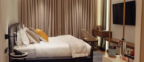 Habitación de hotel con cama, mesita de noche, lámpara, silla, escritorio y televisor de pantalla plana.