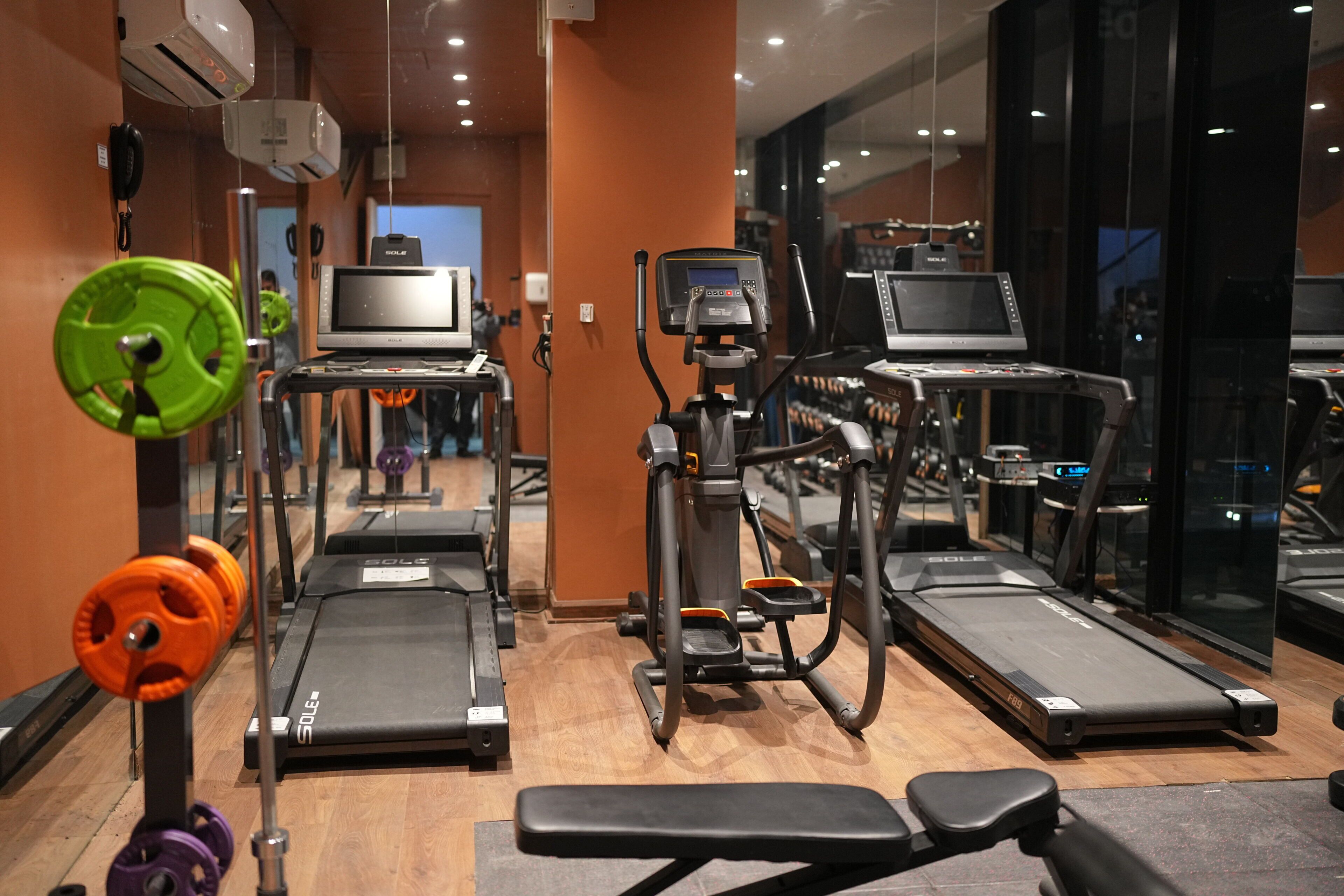 A gym with treadmills, weight machines, and a mirror wall.