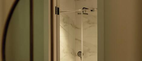 Un baño con cabina de ducha de vidrio, un perchero visible y un espejo que refleja la zona de la ducha.