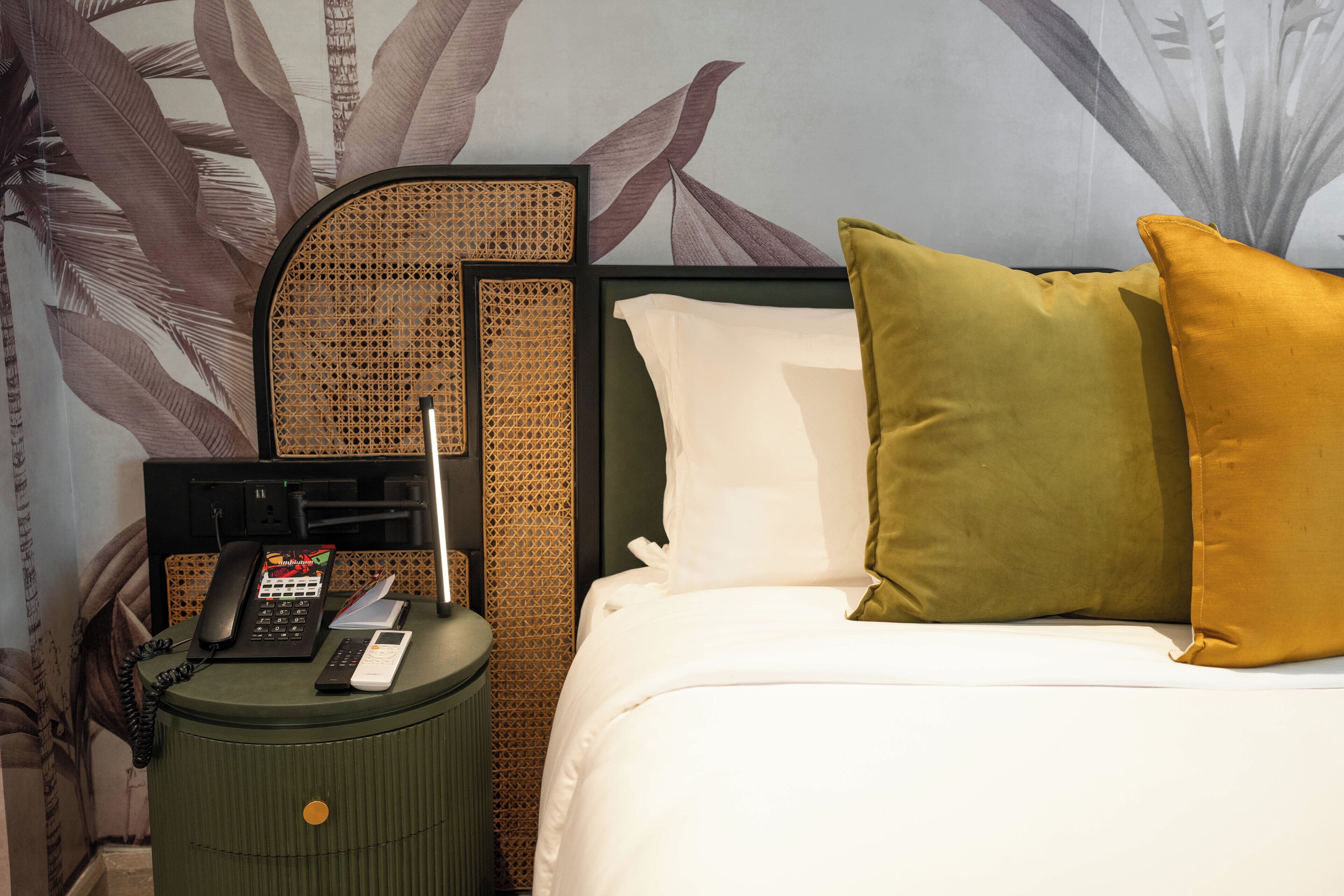 A neatly made bed with white and green pillows, a bedside telephone, and a lamp on a green nightstand.