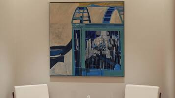 A room with two white chairs, a small round table, and a painting on the wall.