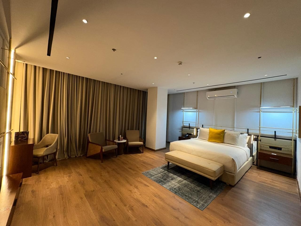 A modern hotel room with a large bed, two armchairs, a small table, and a desk.