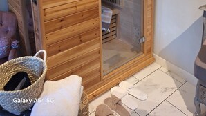 A wooden sauna with a control panel, a glass door, and a bench inside.