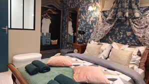 A bedroom with a bed, pillows, a bedside table, a mirror, a wardrobe, and a curtain.