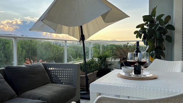 A balcony with a white table, a white chair, a grey sofa, and a large umbrella.