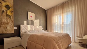 A modern bedroom with a large bed, a bedside table, a chair, and a painting on the wall.