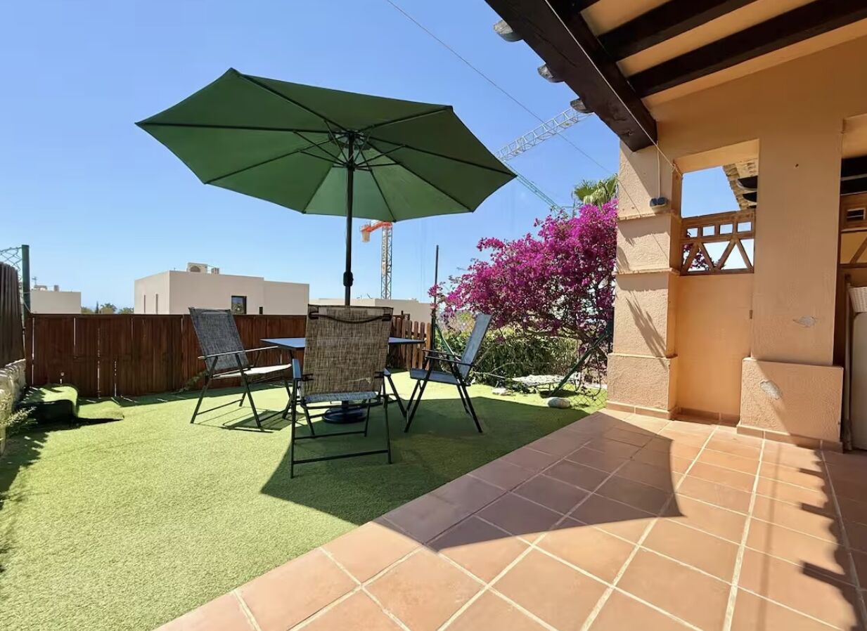 A patio with a green lawn, outdoor furniture, and a large umbrella.