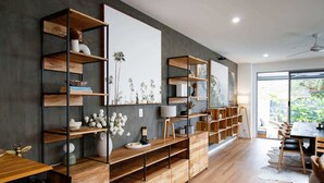 A modern living room with wooden shelves, a dining area, and a large window offering a view of greenery. - Ohana by Khove (Miami)