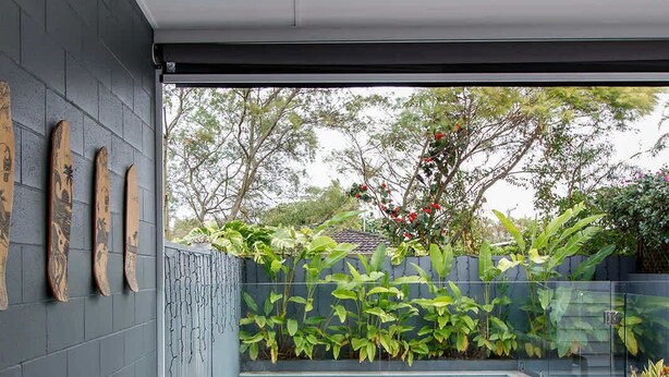 A modern outdoor living area with a grey sofa, wooden coffee table, and lounge chairs. A swimming pool is visible in the background, surrounded by lush greenery. - Ohana by Khove (Miami)