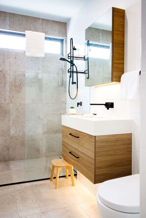 Un bagno moderno con box doccia in vetro, mobile bagno in legno con piano di lavoro bianco e un ampio specchio sopra il lavabo.