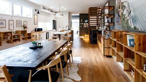 A spacious kitchen with a long wooden table, wooden chairs, and a white cowhide rug. There are wooden shelves on the right and a ceiling fan. - Ohana by Khove (Miami)