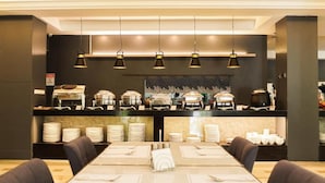 A buffet setup with multiple food stations, a long dining table with chairs, and overhead lighting. - Dancenter Luxury Retreat Angeles City (Angeles City)