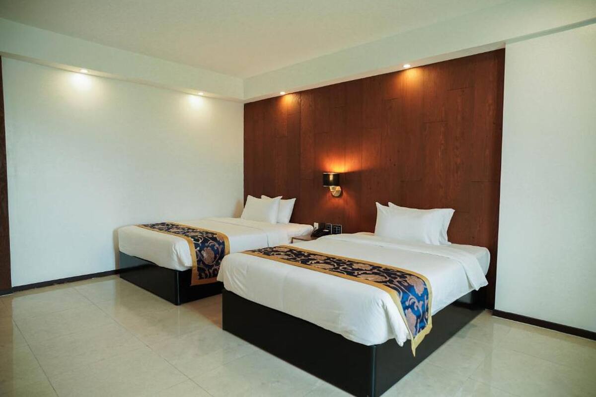 Une chambre d’hôtel avec deux lits, un mur décoratif en bois et un luminaire fixé au mur.