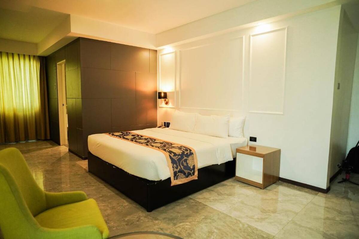 Une chambre d’hôtel avec un lit, une table de chevet, une chaise et une lampe fixée au mur.