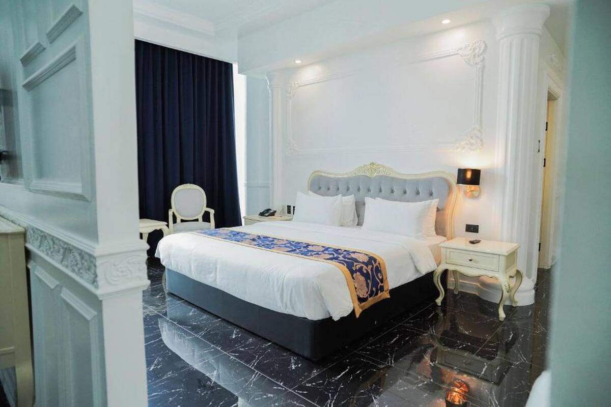 Une chambre d’hôtel avec un grand lit, une table de chevet, une chaise et un rideau foncé.