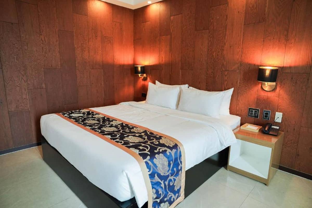 Une chambre d’hôtel avec un grand lit, des murs lambrissés, deux lampes de chevet, une table de chevet avec un téléphone et une petite table d’appoint.