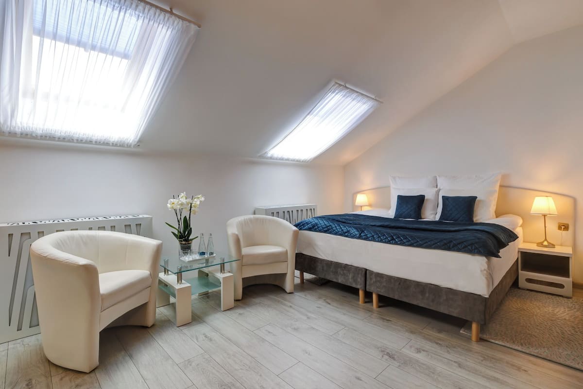 A bedroom with a bed, two chairs, a glass table, and a radiator.