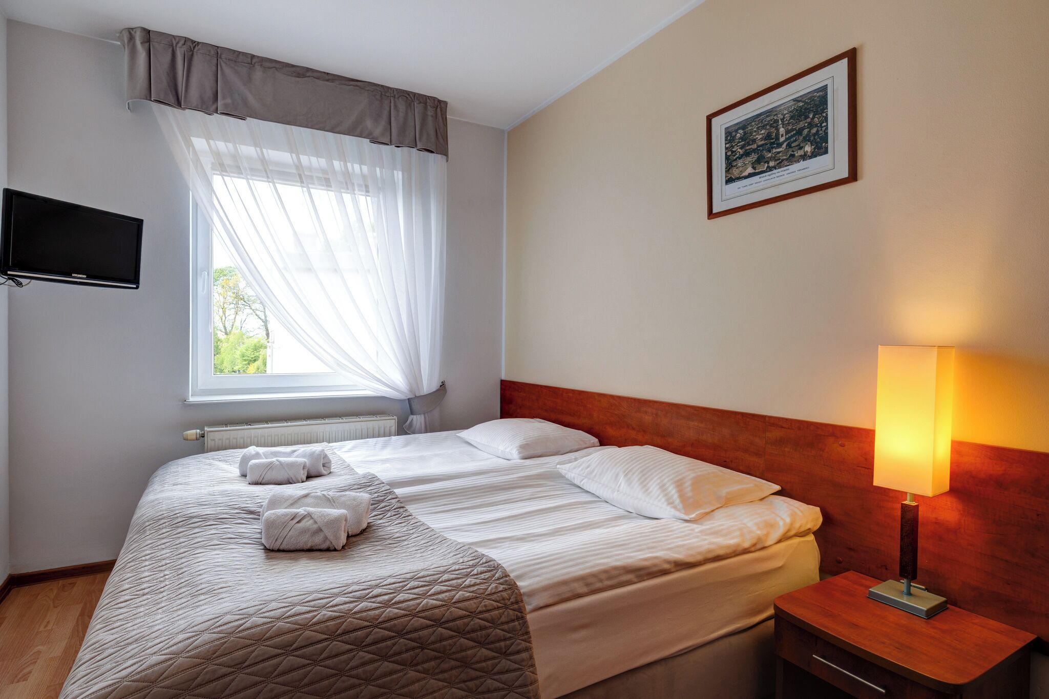 A hotel room with a bed, a bedside lamp, a TV, and a window with curtains.