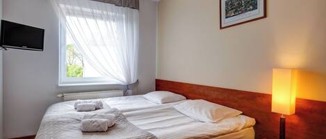 A hotel room with a bed, a bedside lamp, a TV, and a window with curtains.