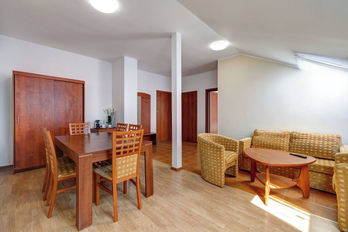 A spacious living room with a wooden dining table and chairs, a patterned sofa, and a small wooden coffee table.