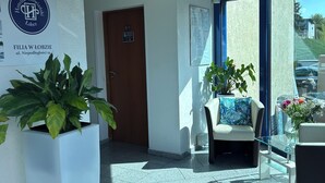 Η είσοδος ενός ξενοδοχείου με μια πινακίδα που υποδεικνύει τον χώρο αναμονής, μια πόρτα και έναν χώρο με καθίσματα, όπου υπάρχει ένα τραπέζι και καρέκλες από γυαλί.