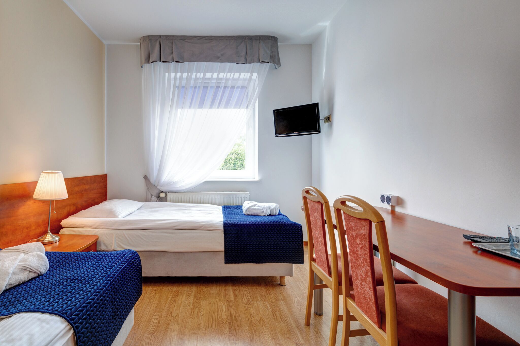 Hotelkamer met een bed, een bureau, een stoel, een televisie en een raam met dunne gordijnen.