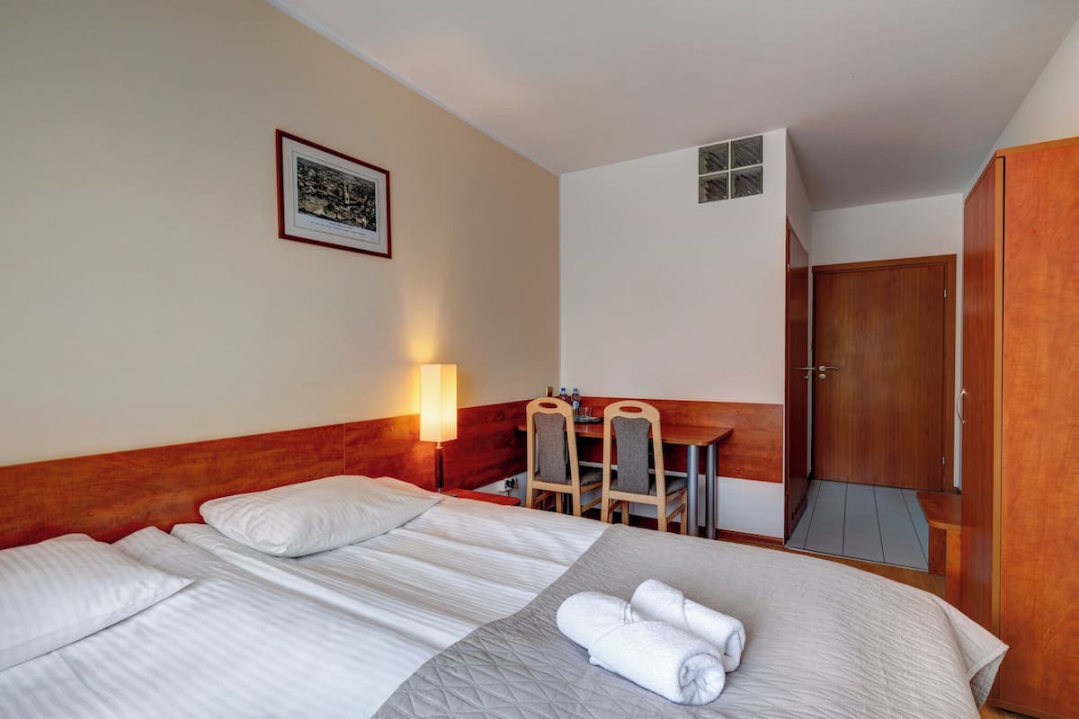 A hotel room with a bed, a desk, and a chair. There is a door and a wall-mounted picture.