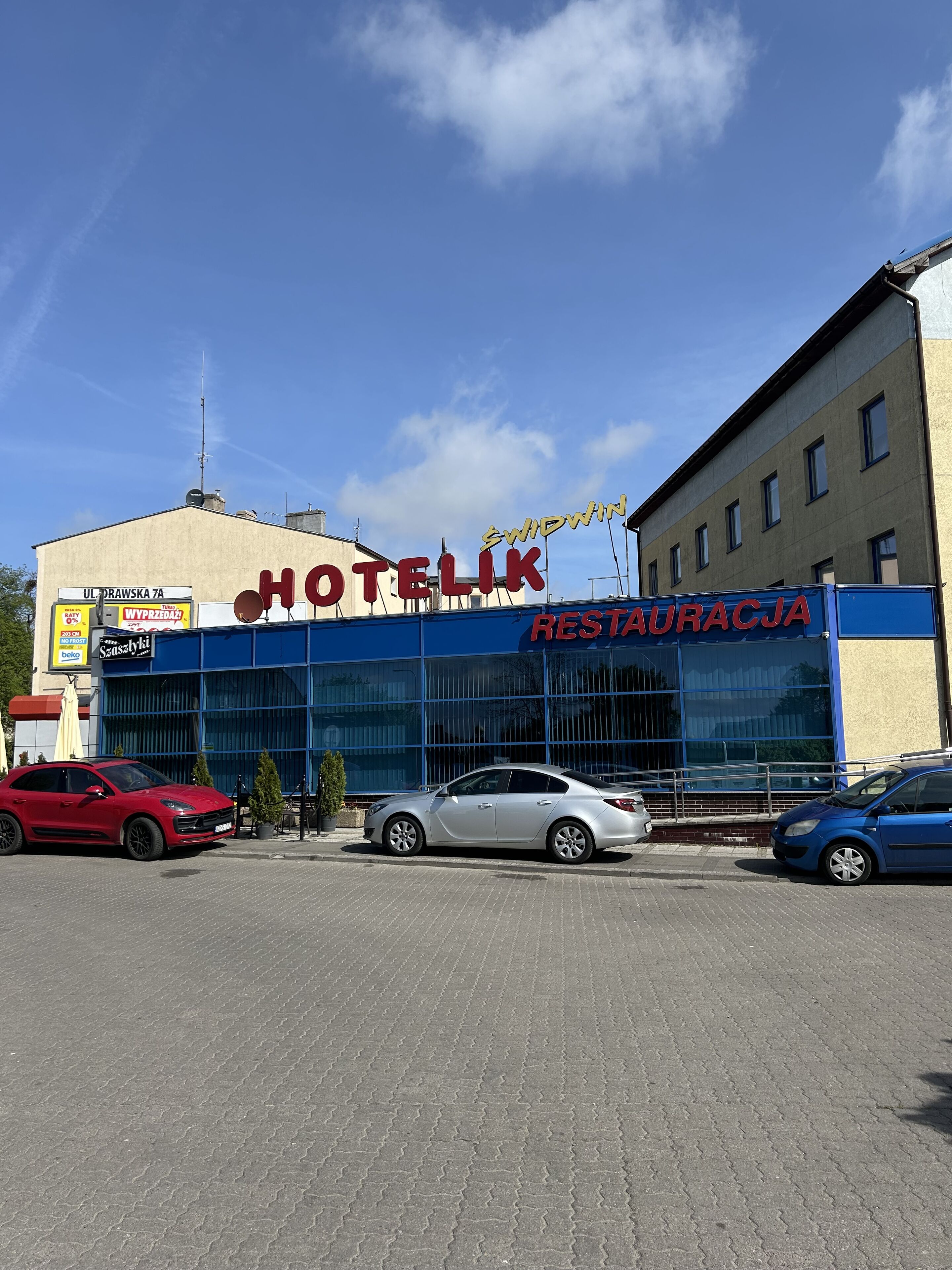 Un hotel con un letrero que dice 'HOTELIK RESTAURACJA' y dos coches estacionados adelante.