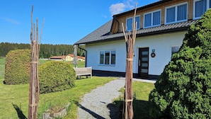 A house with a gravel path leading to the entrance, surrounded by greenery and a clear blue sky.