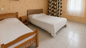 Une chambre avec deux lits, une table de chevet, un climatiseur fixé au mur et une fenêtre avec des rideaux.