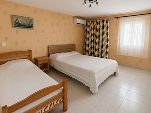 A bedroom with two beds, a nightstand, a wall-mounted air conditioner, and a window with curtains.