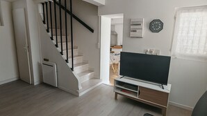 Un salon avec un escalier, un téléviseur à écran plat et une horloge au mur.