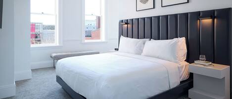 A modern bedroom with a large bed, two bedside tables, and a view of the city through a window.
