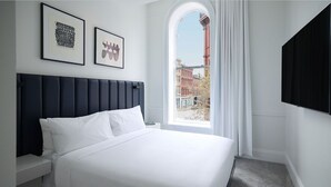 Una camera d'albergo con un letto grande, una testiera, un comodino, una TV a parete e una finestra con vista sugli edifici.