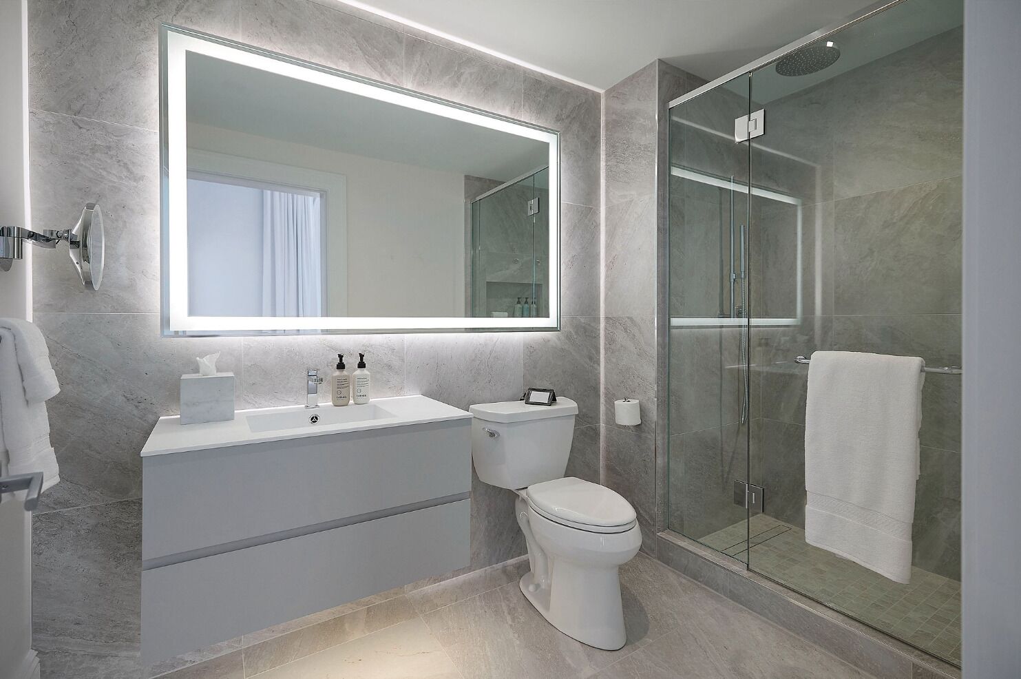 A modern bathroom with a large mirror, a glass-enclosed shower, and a white sink.