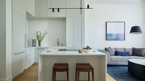 Una cucina moderna con isola centrale, due sgabelli e un'area pranzo con divano e tavolino.
