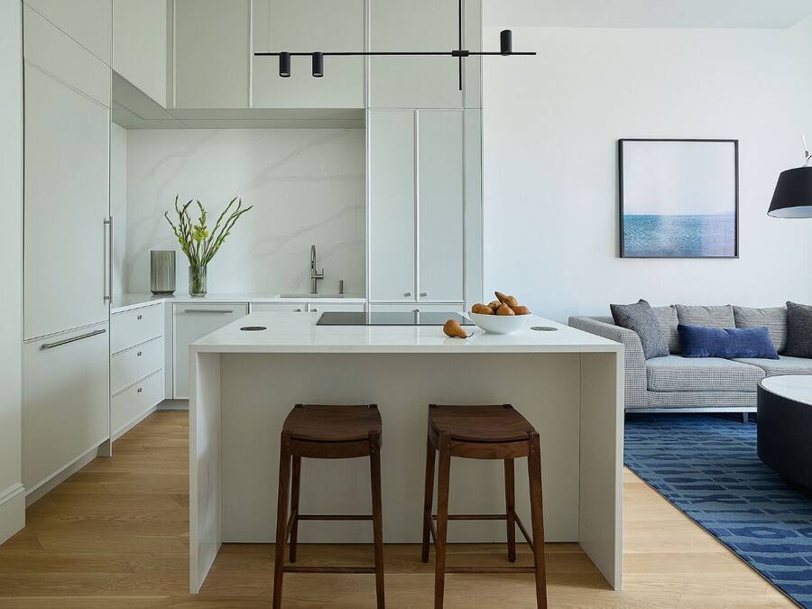 A modern kitchen with a central island, two stools, and a dining area with a sofa and a coffee table.