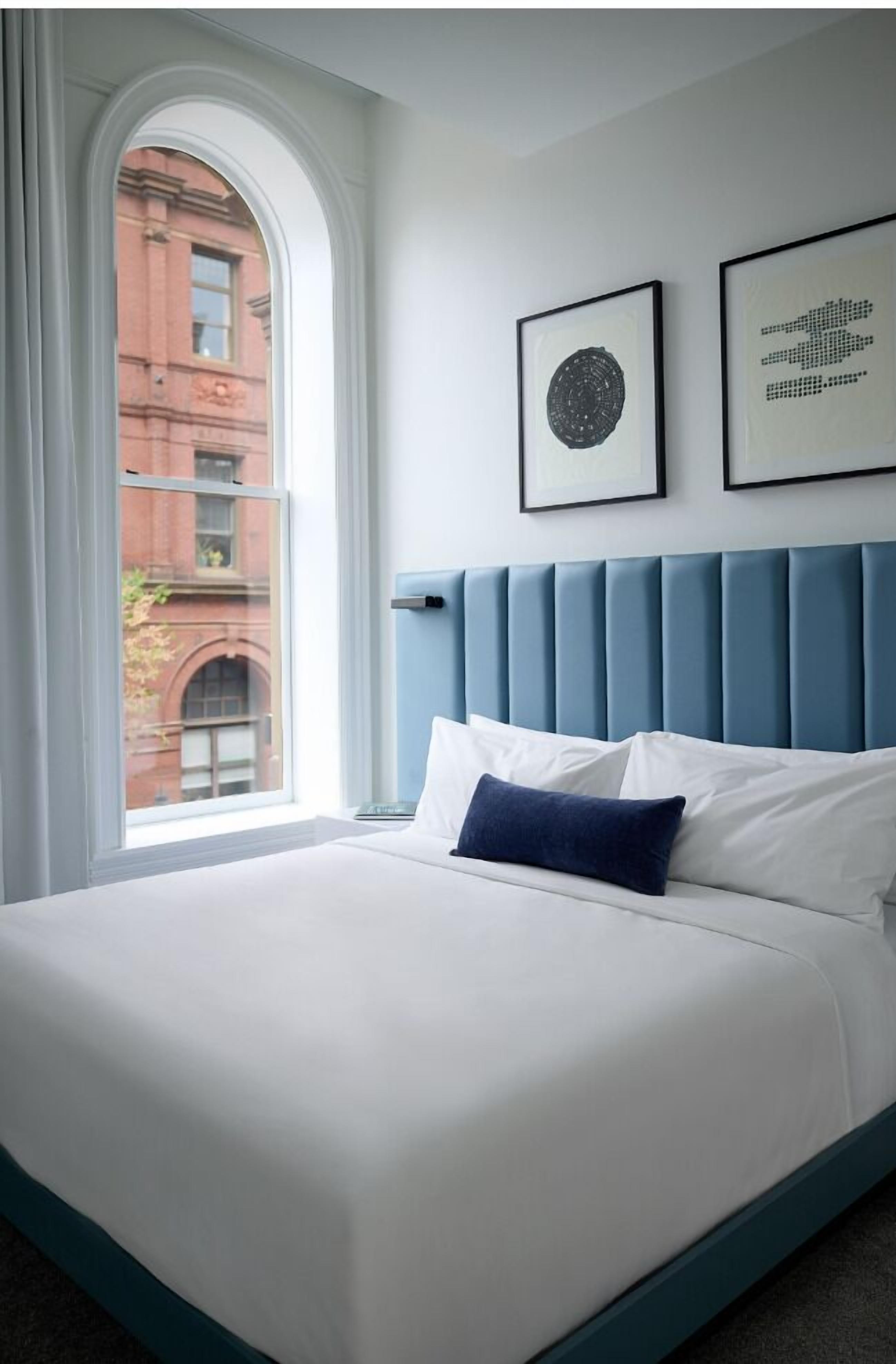 A neatly made bed with white and blue bedding, a blue headboard, and two framed artworks on the wall.