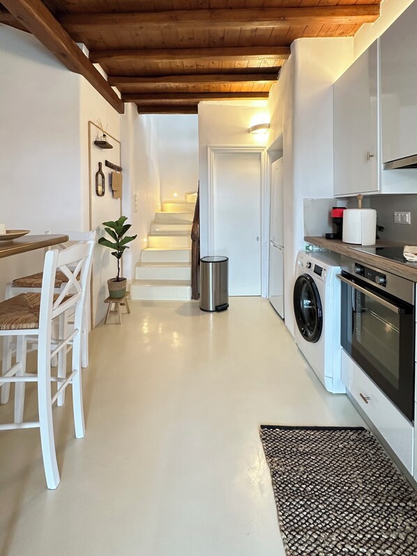 Une cuisine compacte équipée d’un lave-linge, un coin repas avec une table et des chaises, et un escalier menant à une autre pièce.