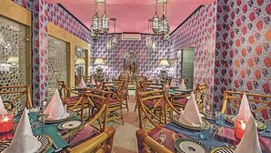 Un coin repas avec un papier peint à motifs, des chaises en bois et des tables dressées pour le repas.