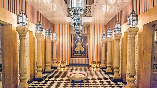 Un vaste hall d’entrée avec un sol à carreaux, des colonnes richement décorées et un arrangement floral central.