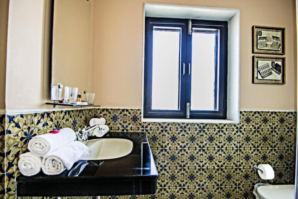 A bathroom with a black sink, a mirror, a window, and patterned tiles.